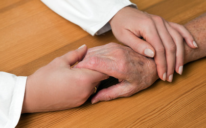 Pflegerin hält die Hände einer Seniorin